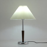 Chrome table lamp with the pleated shade glowing in a dim room