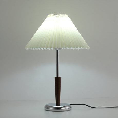 Chrome table lamp with the pleated shade glowing in a dim room