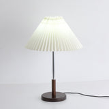 Chrome stem table lamp lit with a cooler light, pleats reading as lines