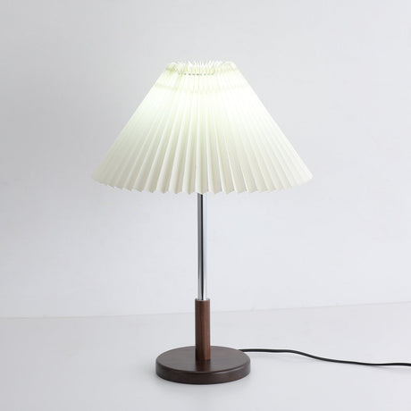 Chrome stem table lamp lit with a cooler light, pleats reading as lines