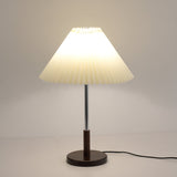 Chrome stem table lamp lit against a pale gray ground, cord to the right