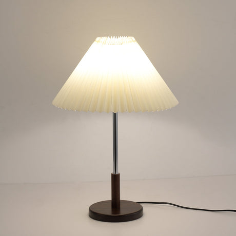 Chrome stem table lamp lit against a pale gray ground, cord to the right