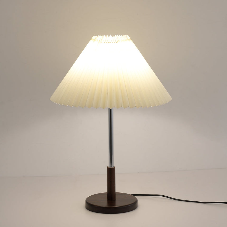 Chrome stem table lamp lit against a pale gray ground, cord to the right