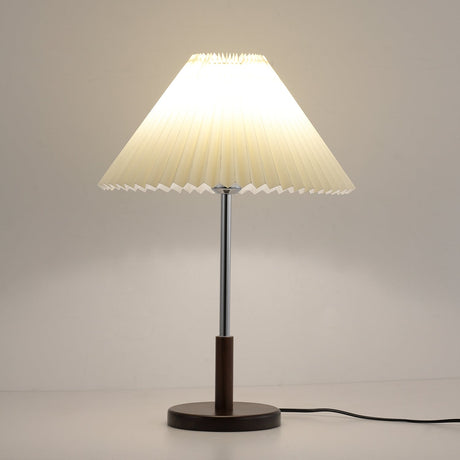 Chrome stem table lamp lit against a warm ground, the shade glowing amber