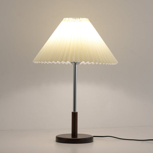 Chrome stem table lamp lit against a warm ground, the shade glowing amber