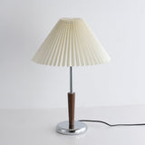 Chrome table lamp seen from the front, pleated shade above the chrome foot