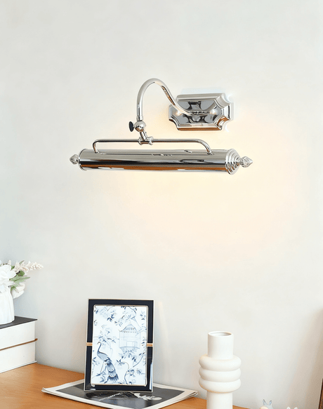 Chrome bar lit over a framed print and a white vase on a wood desk top