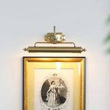 The gold version lit above a gilt framed engraving on a pale wall with a plant