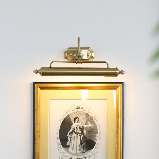 The gold version lit above a gilt framed engraving on a pale wall with a plant