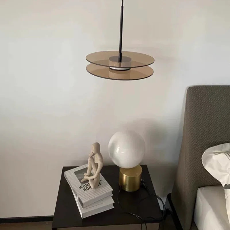 The glass disc lit beside a bed above a table with books and a lamp