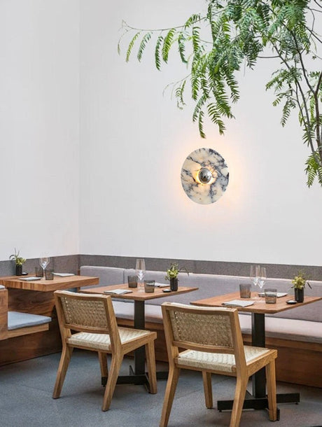 The marble disc lit above a dining table with cane chairs