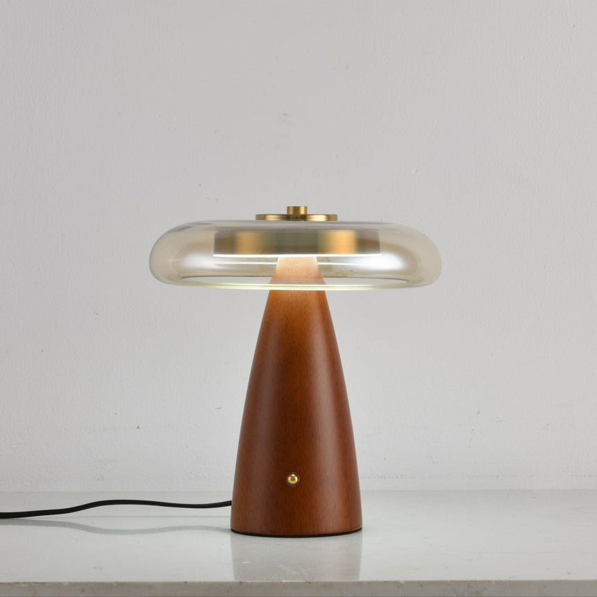Clear glass table lamp on a cone base unlit against a pale ground