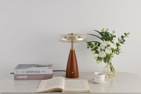 Clear glass table lamp on a cone base beside a vase of flowers