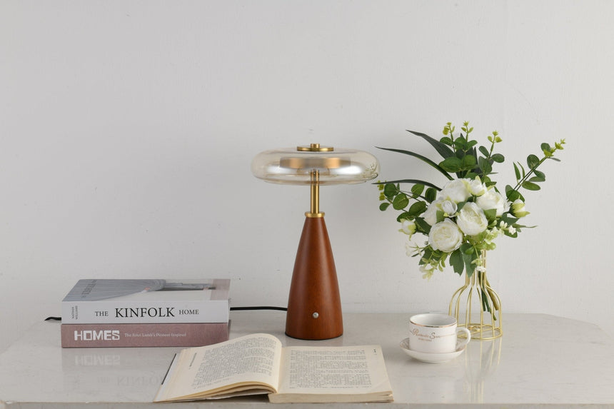 Clear glass table lamp on a cone base beside a vase of flowers