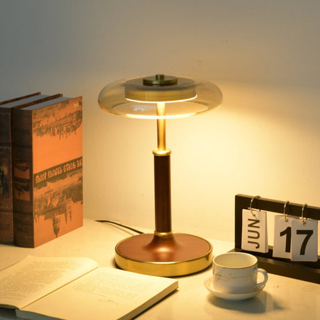 Glass disc lamp lit warm amber above an open book and a cup