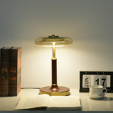 Glass disc lamp lit warm on a desk, the glass catching the glow