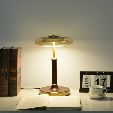 Glass disc lamp lit warm on a desk, the glass catching the glow