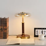 Glass disc lamp lit on a desk beside bound books and a teacup