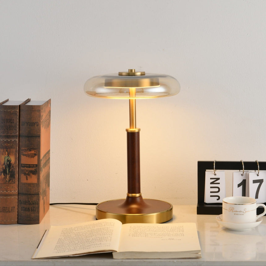 Glass disc lamp lit on a desk beside bound books and a teacup