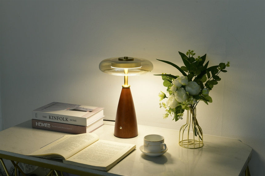 Clear glass table lamp lit on a sideboard in a dim room