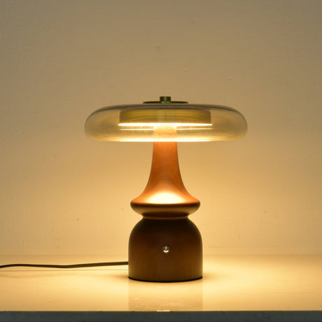 Clear glass table lamp lit against a dark ground, the glass glowing