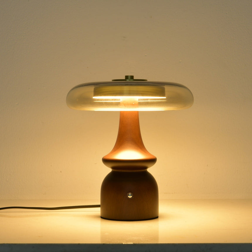 Clear glass table lamp lit against a dark ground, the glass glowing