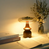 Clear glass table lamp lit warm on a desk beside an open book