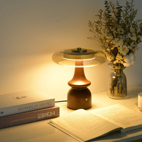 Clear glass table lamp lit warm on a desk beside an open book