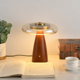Clear glass table lamp lit on a desk beside books and a cup