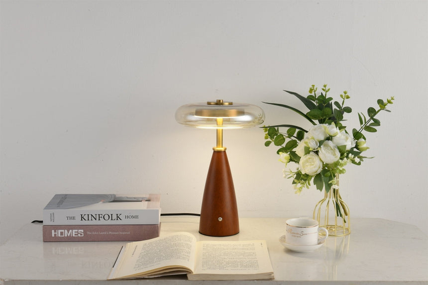 Clear glass table lamp lit on a white table beside white flowers