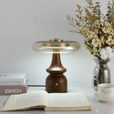 Clear glass table lamp on a spindle base, lit beside flowers