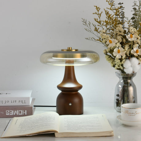 Clear glass table lamp on a spindle base, lit beside flowers