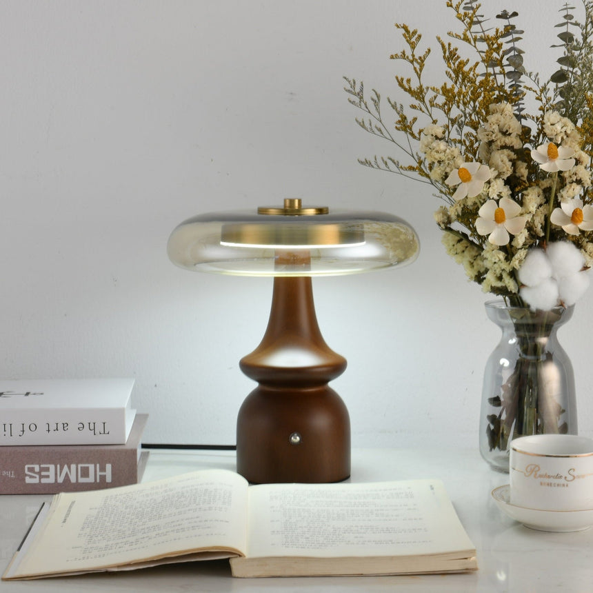 Clear glass table lamp on a spindle base, lit beside flowers