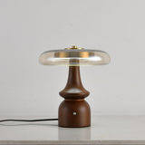 Clear glass table lamp on a spindle base, lit on a plain ground