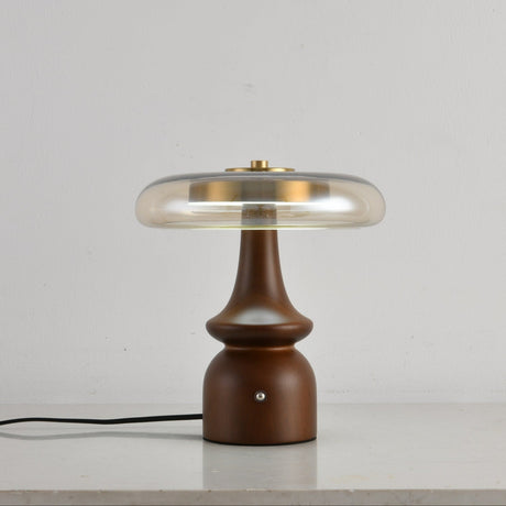 Clear glass table lamp on a spindle base, lit on a plain ground