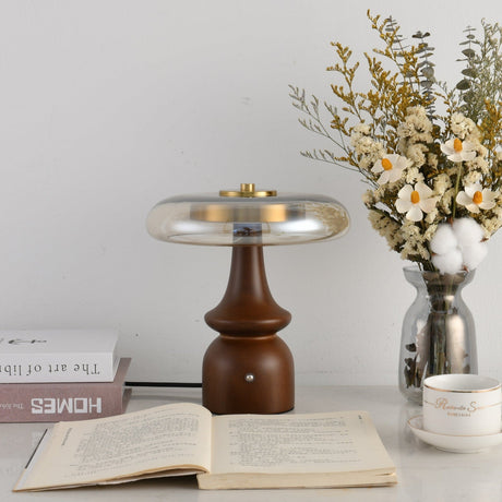Clear glass table lamp lit beside white flowers and old books
