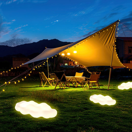 Two lit on grass under a tensioned awning with chairs and string lights