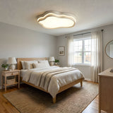 Cloud outline ceiling light above a made bed with cushions in a bedroom finished in warm neutrals