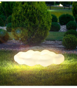 The cloud lit on a lawn beside clipped shrubs in a dark garden