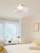White fabric ceiling fixture in a sunlit bedroom with sheer curtains and pale bedding
