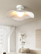 White fabric ceiling fixture lit in a living room with white drapes and a potted plant