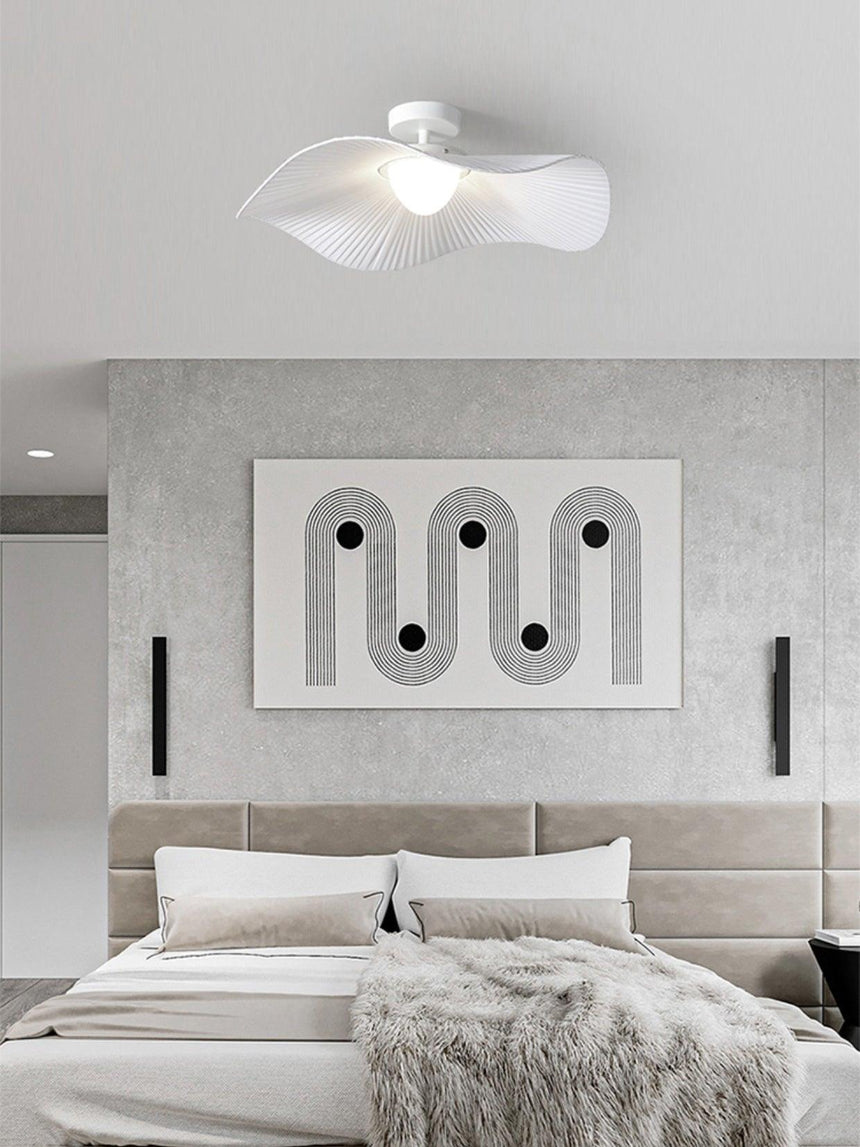 Ceiling light with fabric wings above a bed with a gray headboard and wall art