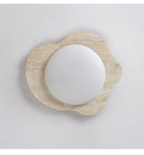 Close view of the unlit travertine frame and the round white lens at its center