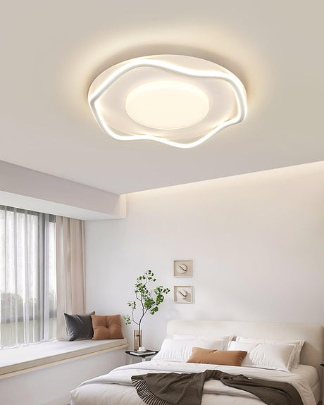 Cloud shaped ceiling lamp lit above a bed with a plant and framed pictures on the wall