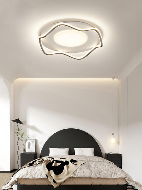 Cloud outline ceiling lamp above a bed with a black headboard and a wall reading light