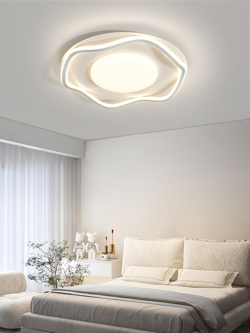 Cloud outline ceiling lamp lit over a bed with white linen and a vase of branches