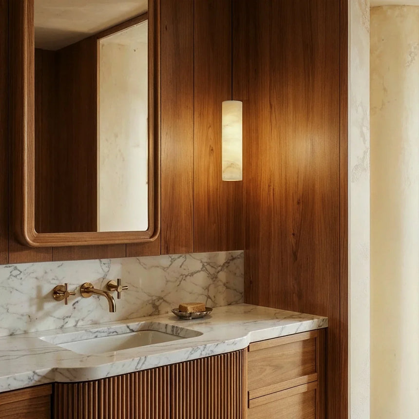 A lit stone cylinder beside a marble vanity and a mirror in a timber bathroom