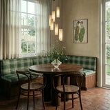 Lit cylinders above a round dining table with chairs and a banquette by a window