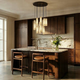 A cluster of lit cylinders above a kitchen island with stools and a marble wall