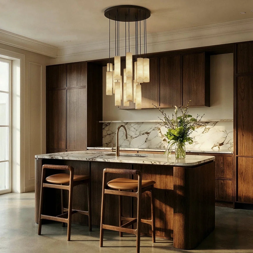 A cluster of lit cylinders above a kitchen island with stools and a marble wall